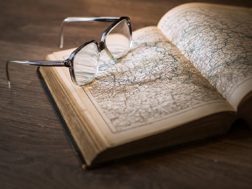 Un vieil atlas avec des lunettes ouvertes posé dessus