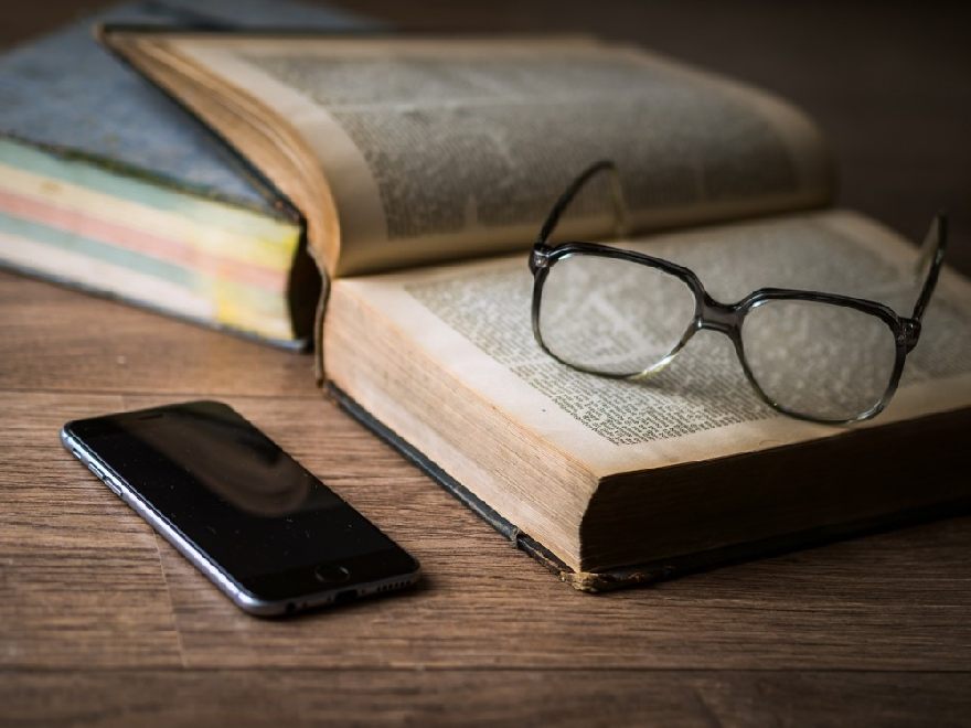 Brille sowie ein aufgeschlagenes Buch und ein Smartphone